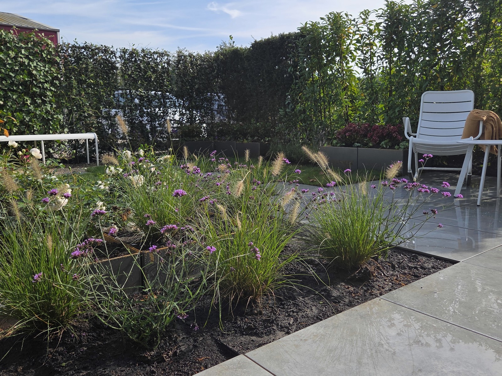 Flowering borders and ornamental grasses next to the terrace with a white garden chair