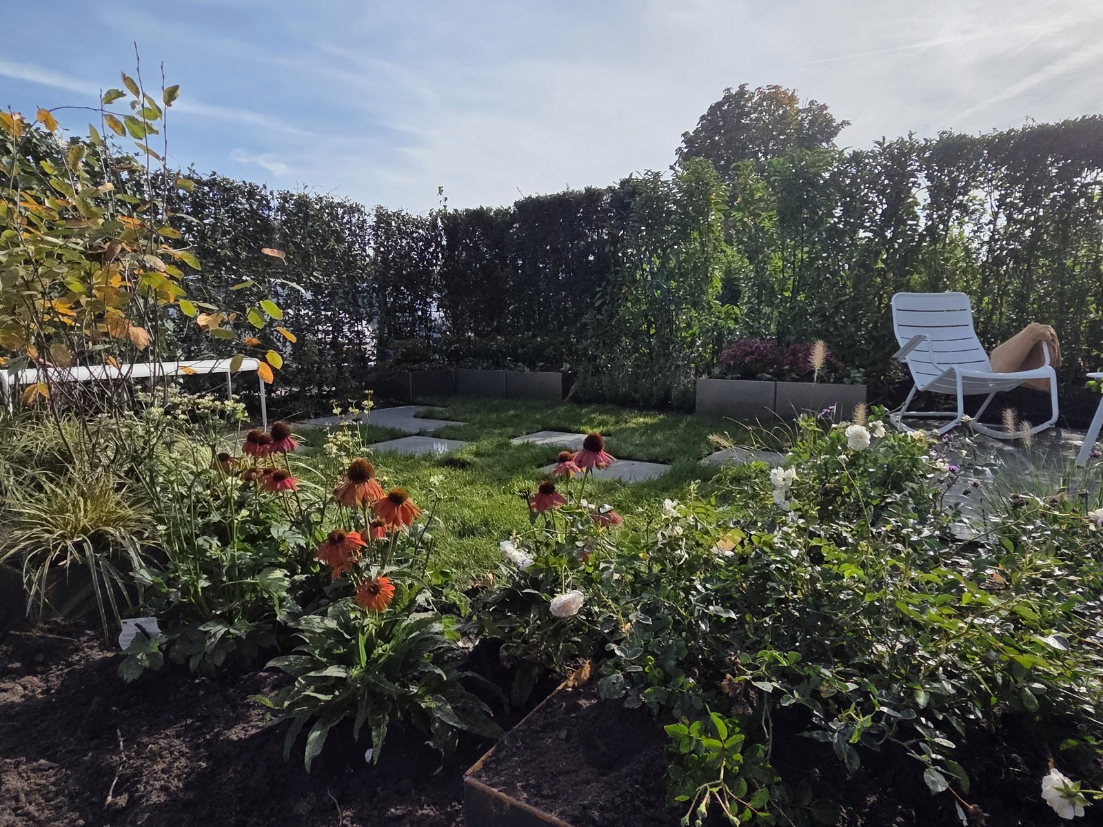 Preverde show garden with flowering borders, grass, stepping stones and a white garden chair